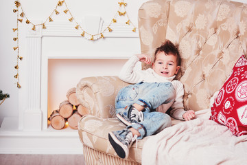 A cute little boy laughs and lies on the couch. A cheerful guy in a knitted sweater and a stylish...