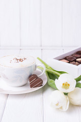 Coffee cappuccino with ceylon cinnamon, luxury chocolates candy and white tulips on a white background