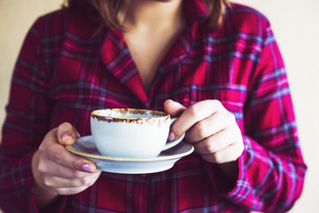 A girl in red checkered pajamas drinks morning tea