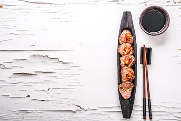 Slices of oriental spicy meat on long dark wooden plate with chopsticks and bowl of sauce, top view