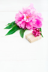 Holiday gift and pink peony on white wooden table with copy space