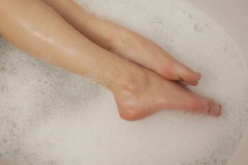 female feet in the tub with water and foam