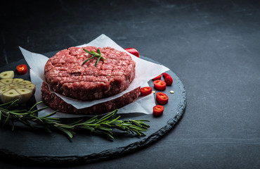 Raw burger cutlet from beef meat with garlic and rosemary on black background with copy space