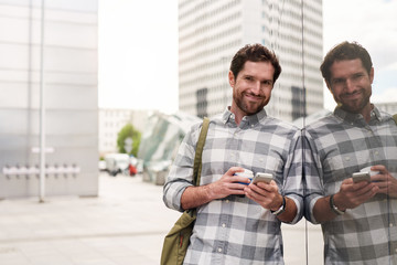 Smiling young man standing in the city using his cellphone