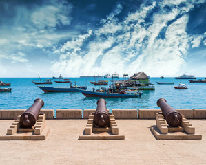 embankment with guns in Zanzibar Stone Town with boats in ocean and sky on the background - obrazy, fototapety, plakaty