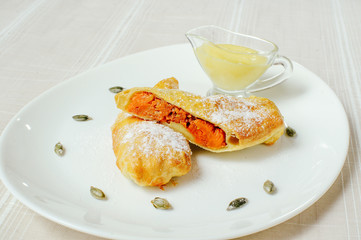 a pumpkin pie with sugar powder and sweet sauce in a white plate, a cozy light table setting, a restaurant feed