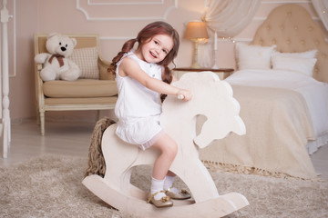 A little girl in her room, the bedroom rocks on a wooden horse. A child on a rocking-chair, in a...