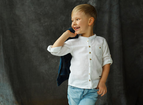 Portrait of little smiley pretty boy in jeans over grey textile background
