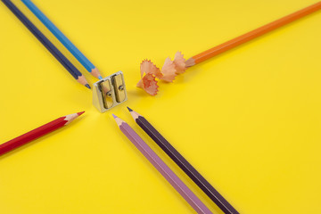 Some colored pencils of different colors and a pencil sharpener and pencil shavings on а yellow background