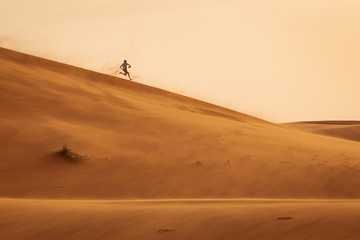 Fototapeta na wymiar Man running joyfuly on dunes of desert Sahara in Morocco in a storm day