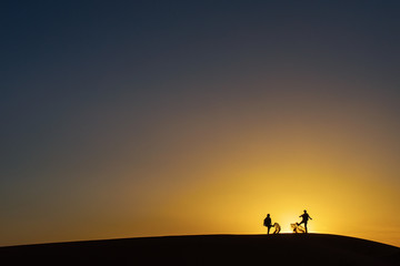 Fototapeta na wymiar Silhouette of two people playing with sands in desert sahara with sunset in background