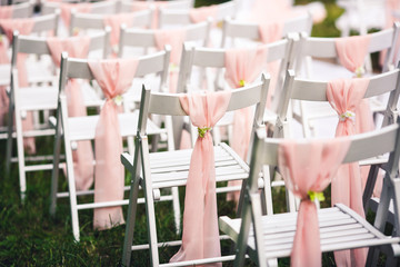 White chairs at the wedding ceremony, decorated with a pink cloth.