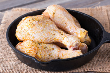 Raw chicken legs in a frying pan on a wooden table. Meat ingredients for cooking.