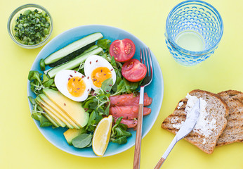  Healthy salad with avocado, corn salad, smoky salmon, eggs and tomatoes for breakfast. Top view. Flat lay. Close up