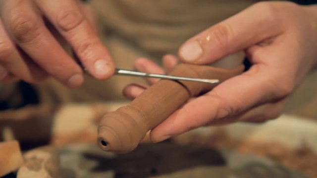 A clay spoon during polishing by a metal bar. 