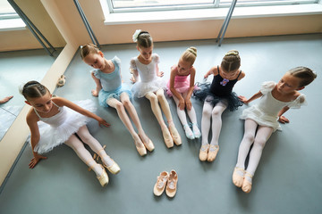 Six ballerinas sitting on floor, top view. Pair of slippers for little ballet girl. Group of young...
