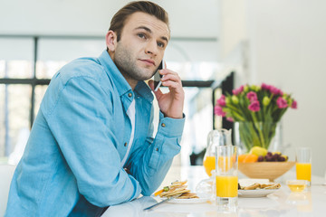 portrait of man talking on smartphone during breakfast at home