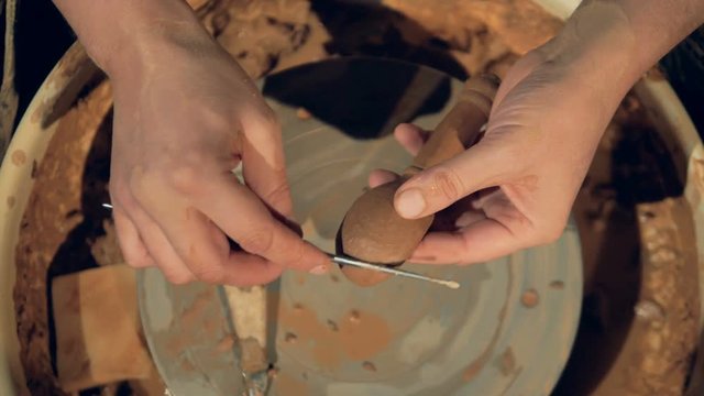 Potters hands use a metal bar to polish a clay spoon. 