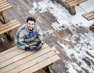 Handsome young man in skiing suit relaxing, sitting at table outside ski resort