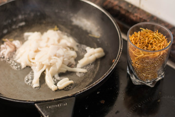 Frying squid in the pan and fideua noodles in a glass, process of making fideua