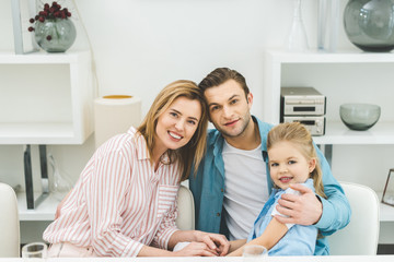 portrait of smiling parents and daughter looking at camera at home