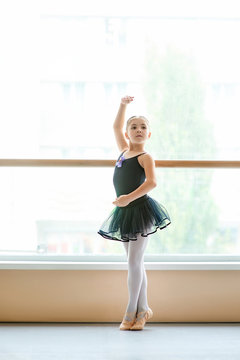 Beautiful ballet girl standing in ballet pose. Pretty young ballerina in black dress posing in ballet class.