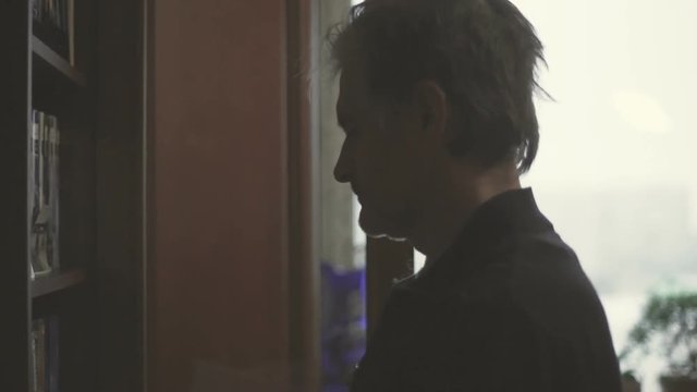 Ederly man chooses a book to read against the window video
