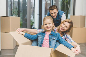 portrait of smiling parents and little daughter in cardboard box at new home, moving home concept