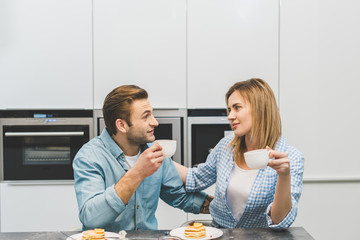 portrait of couple with cups of coffee in kitchen at home