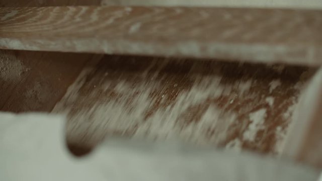 Wheat grain that was pulvered into flour inside a windmill flows through a wooden beam and falls into a bag while the shadow of the sails of the mill darkens the image, shot in 50fps slowmotion
