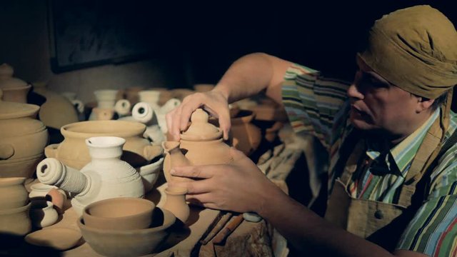 A potter removes a from inside a clay teapot. 