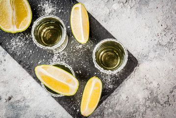 Tequila shots with lime and sea salt on grey stone table, copy space