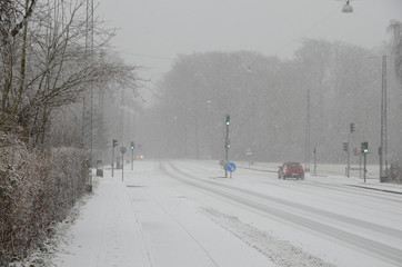 Sparce traffic moving slowly, on a road during heavy snowfall that causes reduced visibility.