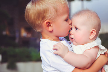 happy little brother playing hugs his sister baby, boy and girl embraces kisses, concept love and parenting