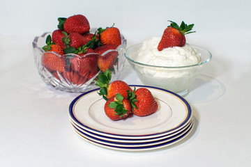 A bowl of strawberries, whipped cream and plates
