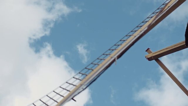 The open sails of an old Dutch pumping windmill fly by from top to bottom in front of a blue sky on a sunny summer day with some clouds in the sky shot in 50fps slowmotion