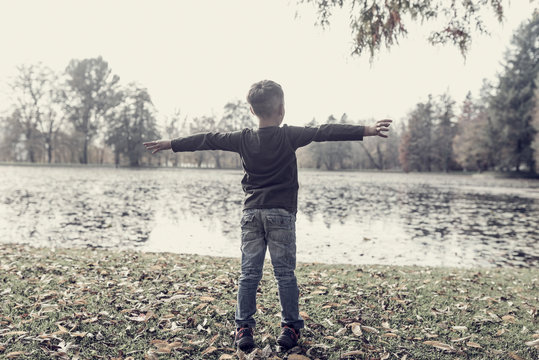 Young child enjoying the autumn weather standing with outstretched arms