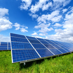 Solar panel on blue sky background. Green grass and cloudy sky. Alternative energy concept
