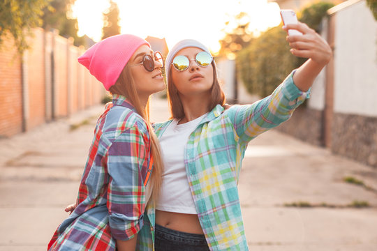 Two girls take pictures of themselves on the phone at evening in the city
