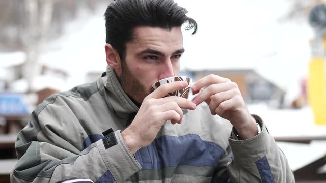 Handsome young man in skiing suit relaxing with cup of coffee looking pensively away.