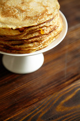 Stack of pancakes with orange jam and honey on white cake stand on wooden table. Pancake breakfast concept