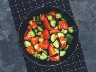 Fresh cucumber tomato salad on black background. Healthy food. A vegetarian salad. Fresh vegetables. Top view. Dark moody