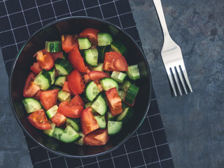 Fresh cucumber tomato salad on black background. Healthy food. A vegetarian salad. Fresh vegetables. Top view. Dark moody