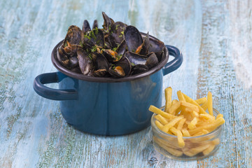 mussels in a blue ceramic pot on a blue wooden background. with a glass bowl of french fries. Brlgium lifestyle.
