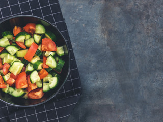 Fresh cucumber tomato salad on black background. Healthy food. A vegetarian salad. Fresh vegetables. Top view. Dark moody