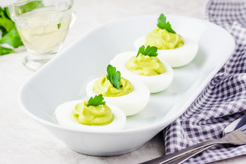 Spring easter holiday appetizer, avocado devilled eggs with parsley on white background. Selective focus, space for text.