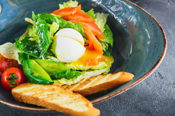 Caesar salad with egg, salmon, avocado, cherry tomatoes and grilled bread, close up view