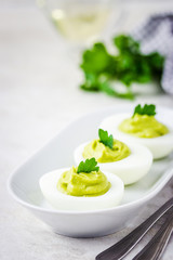 Spring easter holiday appetizer, avocado devilled eggs with parsley on white background. Selective focus, space for text.