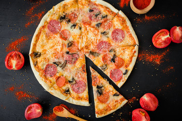 Pizza with salami, tomato and cheese on dark table. Flat lay, top view.
