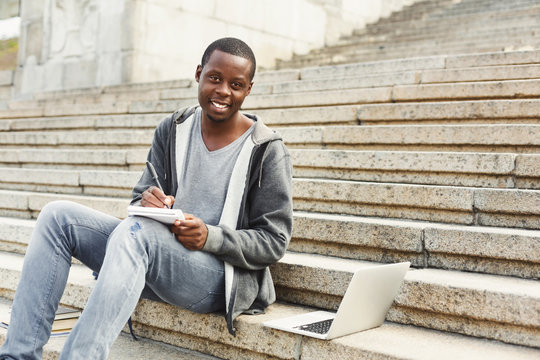 Attractive african-american student making notes sitting on stairs outdoors - Powered by Adobe